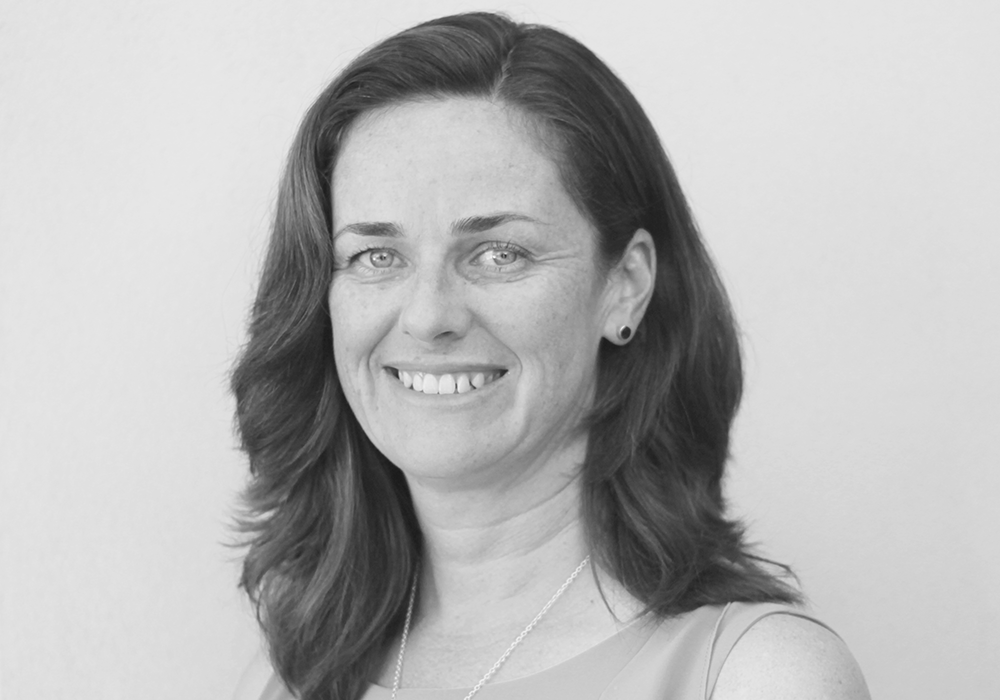 Photo of a woman with dark hair and a necklace. She is smiling at the camera.